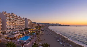 Vista panorámica de una ciudad costera española al atardecer, apartamentos de lujo y hoteles con vistas al mar Mediterráneo, reflejando inversión inmobiliaria turística.
