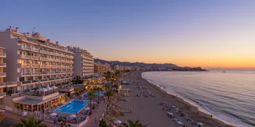 Vista panorámica de una ciudad costera española al atardecer, apartamentos de lujo y hoteles con vistas al mar Mediterráneo, reflejando inversión inmobiliaria turística.
